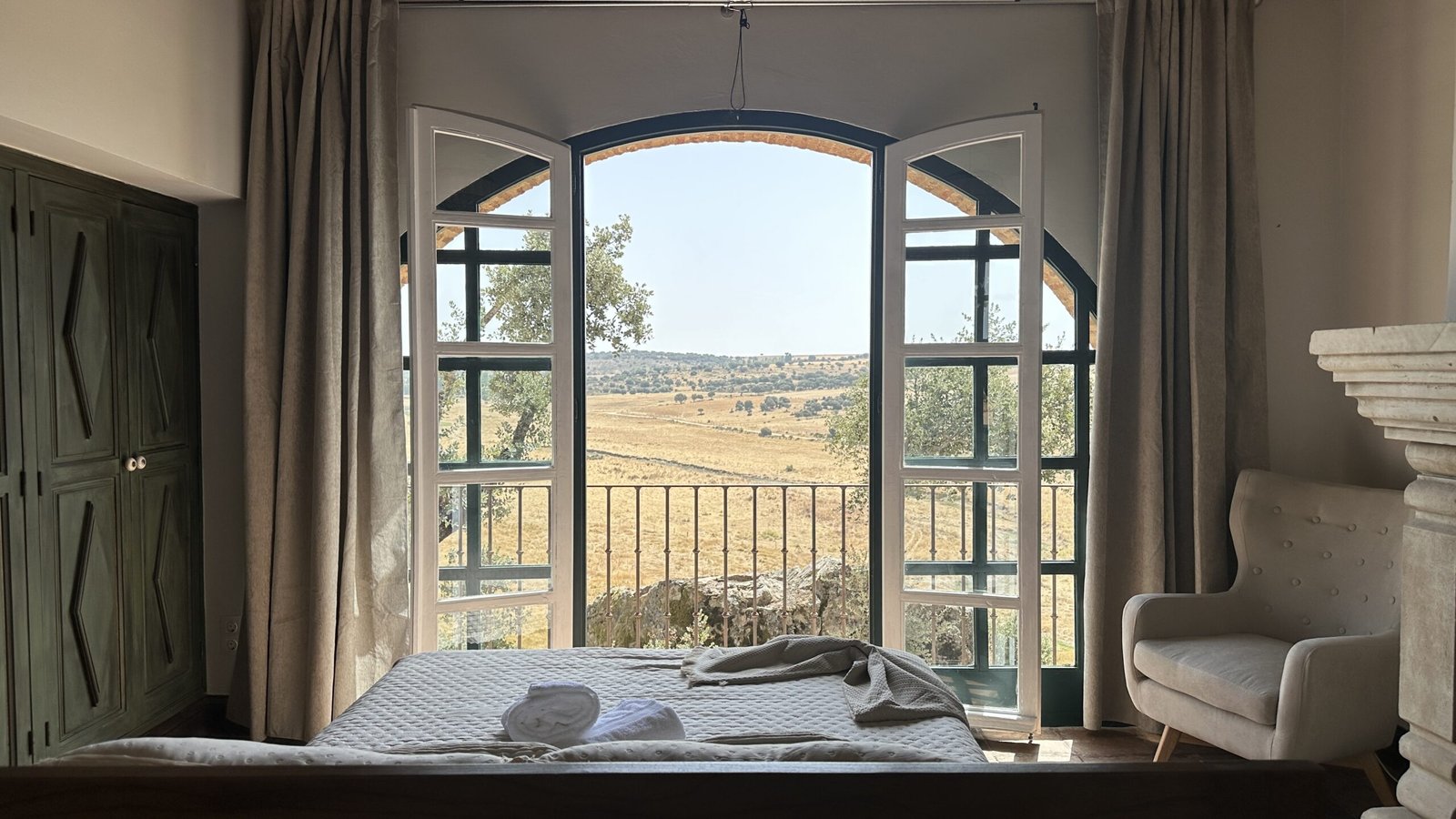 Habitación de La Quintina con cama mirando al ventanal abierto y vistas al campo, con toallas preparadas para los huéspedes, en San Pelayo de Guareña, Salamanca.