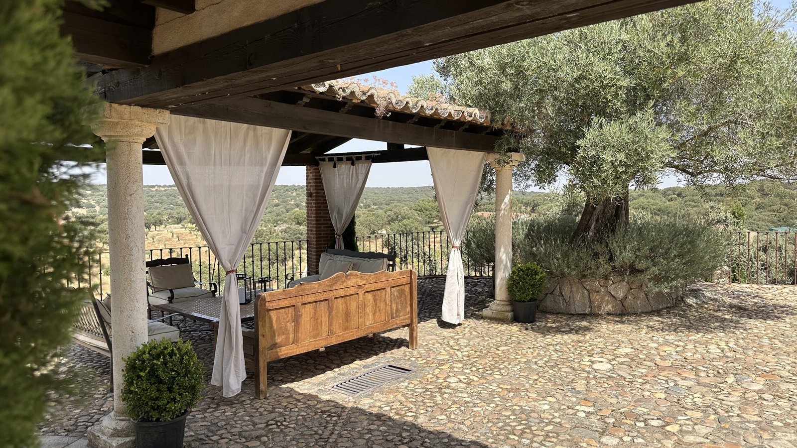 Terraza exterior de La Quintina, casa rural en San Pelayo de Guareña, con tres bancos alrededor de una mesa baja, árbol a la derecha y vistas al campo abierto.